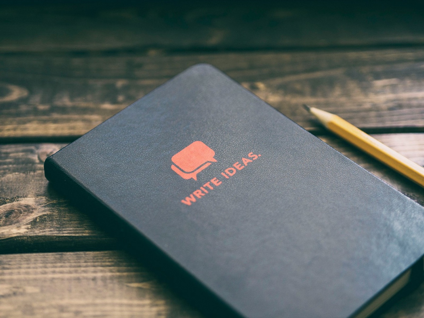 A dark notebook with WRITE IDEAS printed on the cover, next to a pencil