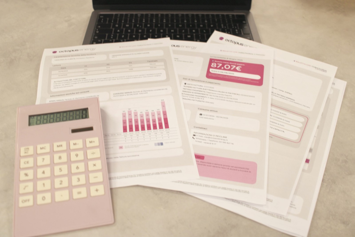 Printed bills spread on a desk next to a calculator and a laptop