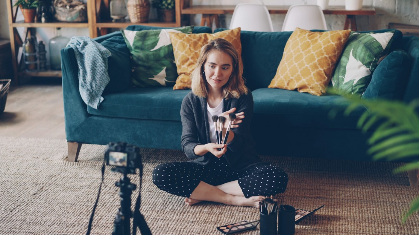 A woman sitting on the floor of her living room, recording a video lesson on a camera